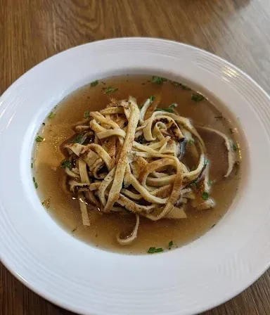 Ein weißer Teller mit Suppe und Nudeln auf einem Holztisch.