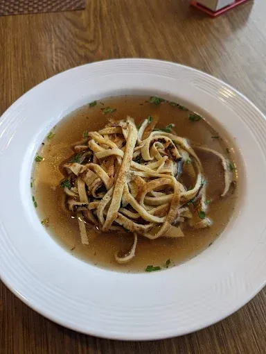 Ein weißer Teller mit Suppe und Nudeln auf einem Holztisch.