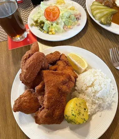 Eine Mahlzeit mit gebratenem Huhn, Reis und Salat. Ein Glas Bier und eine Zitrone auf der Seite.