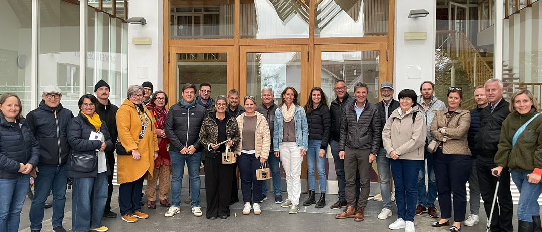 Eine Gruppe von Menschen in Winterkleidung steht vor einem modernen Gebäude mit Glastüren und hölzerne Rahmen.