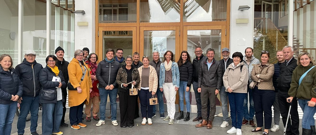 Eine Gruppe von Menschen in Winterkleidung steht vor einem modernen Gebäude mit Glastüren und hölzerne Rahmen.