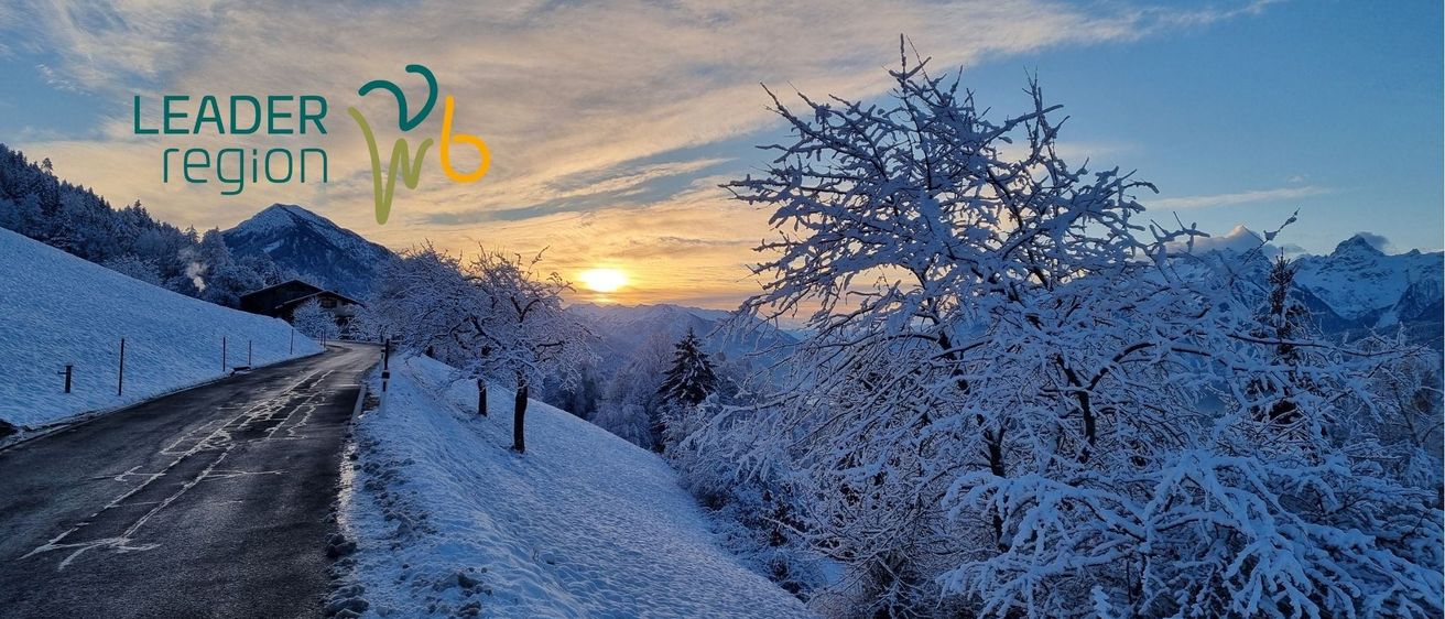 A snowy mountain landscape with trees covered in snow, the sun setting on the horizon with a blue sky.