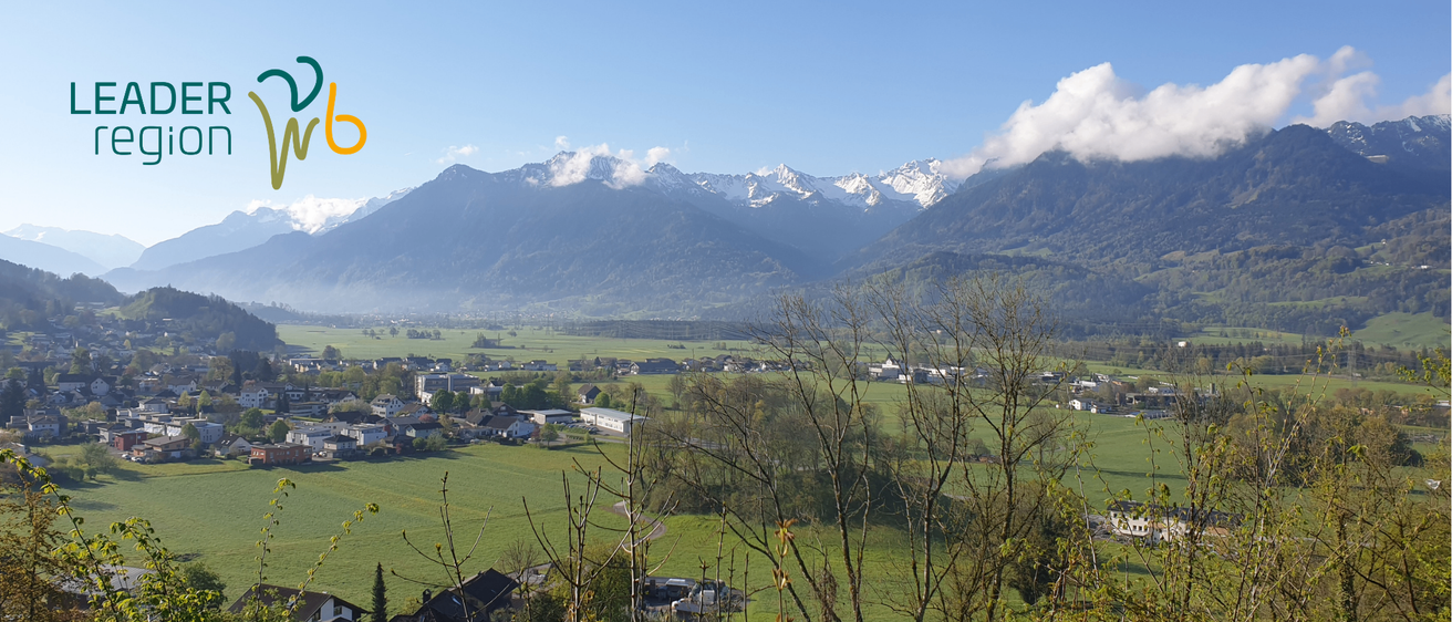 Ein Panoramablick auf ein Tal mit Bergen im Hintergrund, Häuser im Vordergrund und einem klaren blauen Himmel.