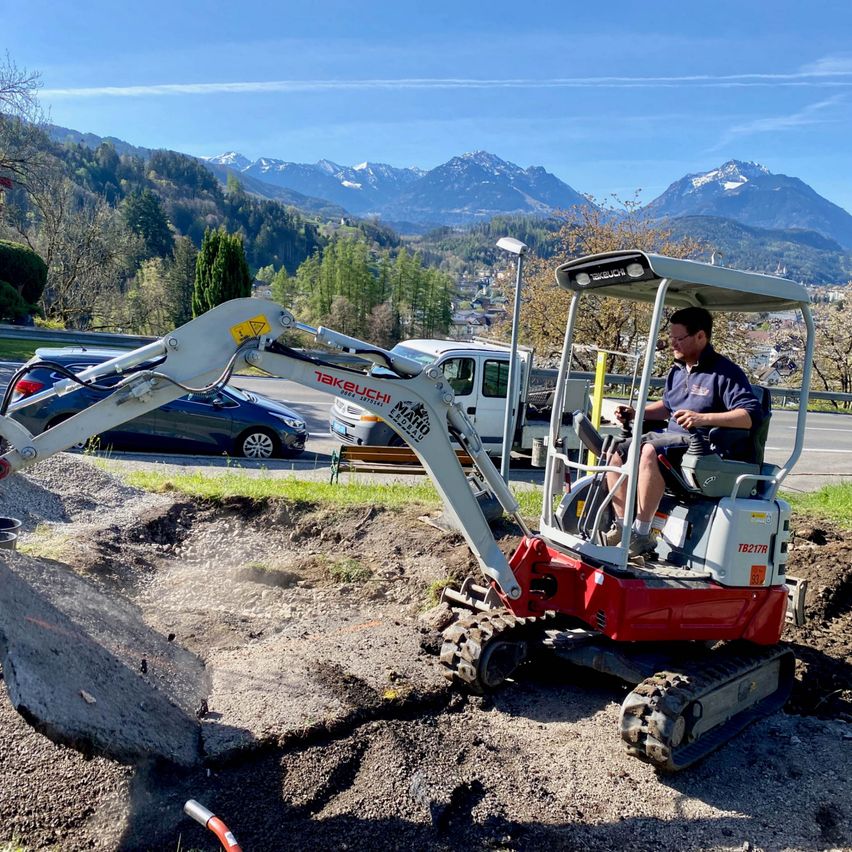 Ein Mann fährt einen Takeuchi-Bagger auf einer Baustelle mit Bergen im Hintergrund.