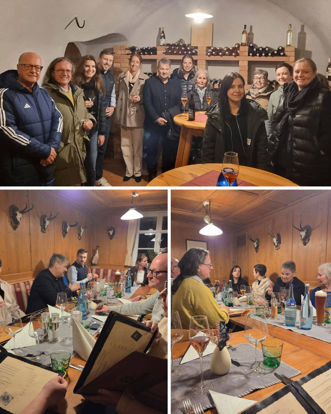 Eine Gruppe von Menschen versammelt sich in einem Raum, einige stehen und andere sitzen um einen Tisch mit Gläsern und Flaschen. Zwei Frauen lächeln, eine mit einem Getränk, während andere zusehen.