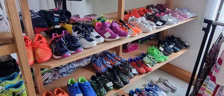 Ein Raum mit Holzregalen, die mit verschiedenen Sportschuhen gefüllt sind, einige an Kleiderbügeln, in Reihen angeordnet. Die Schuhe sind in verschiedenen Farben und Größen.