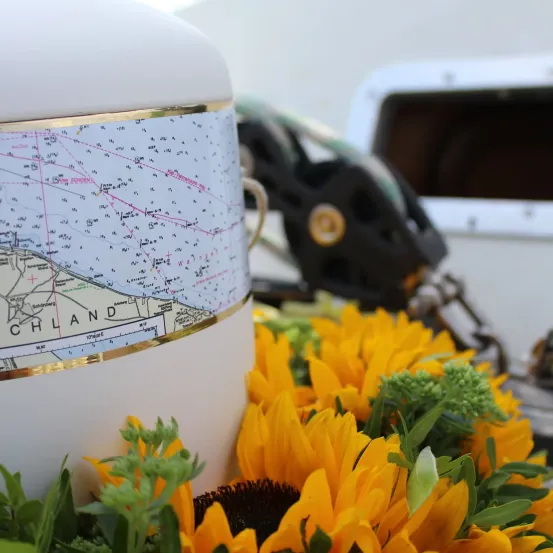 Eine Nahaufnahme einer Seekarte mit einer Blumenarrangement im Vordergrund, bestehend aus Sonnenblumen und Grünpflanzen. Die Karte hat einen goldenen Rand und ist auf einem weißen Behälter montiert.