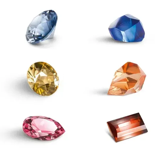 Eine Sammlung verschiedener farbiger Edelsteine wird auf einem weißen Hintergrund gezeigt. Die Edelsteine umfassen Blau, Gelb, Rosa und Rot.