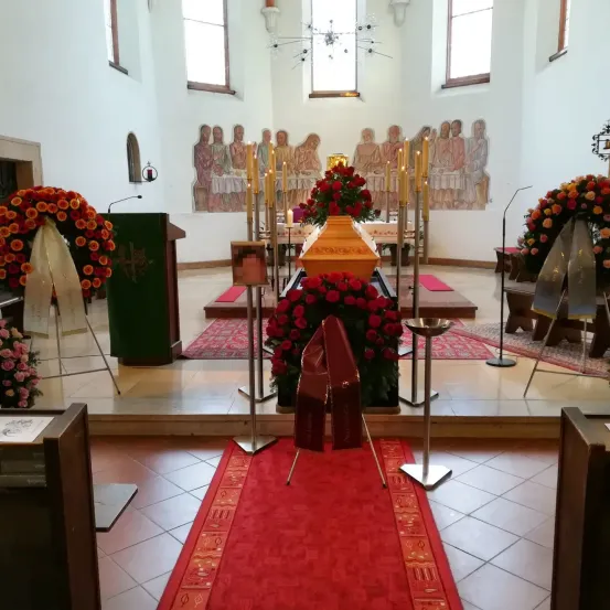 Ein Altar mit einem Sarg bei einer Kirchenbegräbnis, umgeben von Kerzen und Blumen. Zwei lange rote Teppiche führen zum Altar.