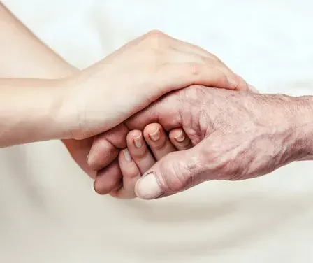 Ein älterer Mann hält die Hand eines Kindes und zeigt eine enge Verbindung. Beide Hände sind leicht faltig, der Hintergrund ist weiß.