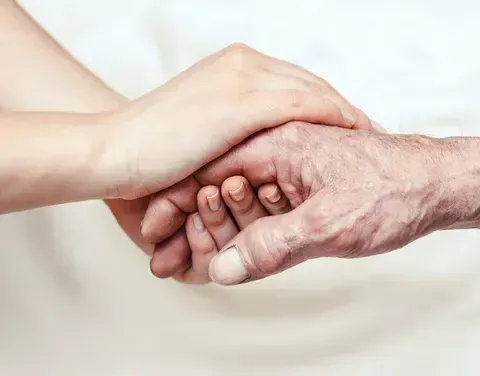 Ein älterer Mann hält die Hand eines Kindes und zeigt eine enge Verbindung. Beide Hände sind leicht faltig, der Hintergrund ist weiß.