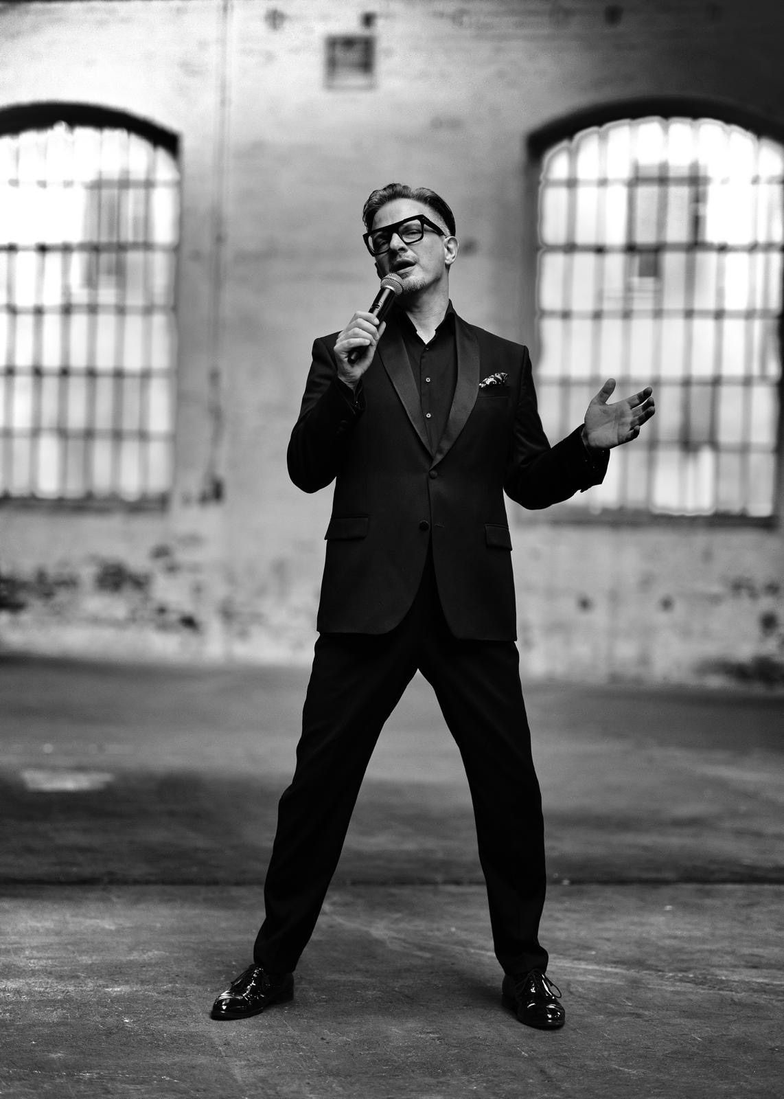 Ein Schwarz-Weiß-Foto eines Mannes in Anzug, der ein Mikrofon hält und in einem leeren Raum singt.