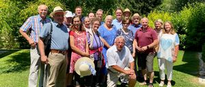 Eine Gruppe von Menschen, darunter Erwachsene und Senioren, posiert für ein Foto im Garten, einige stehend, andere sitzend, mit einem Mix aus Lächeln und ernsten Gesichtern.