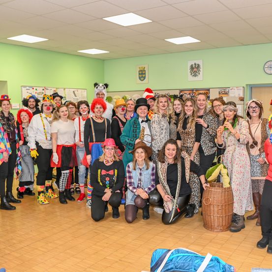 Eine Gruppe von Menschen in Kostümen posiert für ein Foto in einem grünen Raum mit einer Uhr an der Wand.