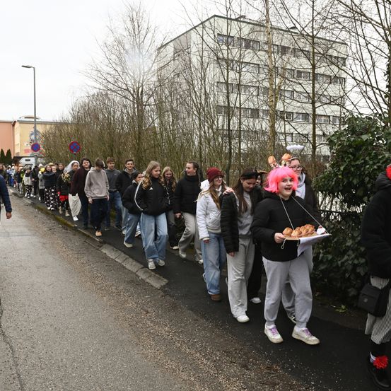 Eine Gruppe von Menschen in Kostümen, einige mit rosa Perücken, gehen auf einer Straße, wahrscheinlich für ein Halloween-Event.
