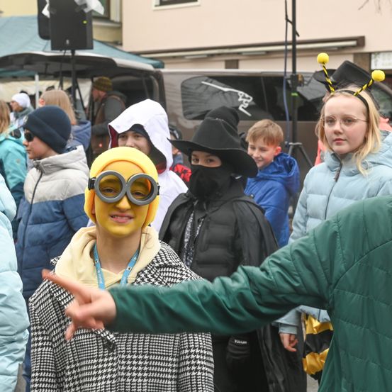 Eine Gruppe von Menschen in verschiedenen Kostümen, darunter eine Biene und ein Minion, steht in einer Menschenmenge draußen. Der Minion zeigt auf etwas.