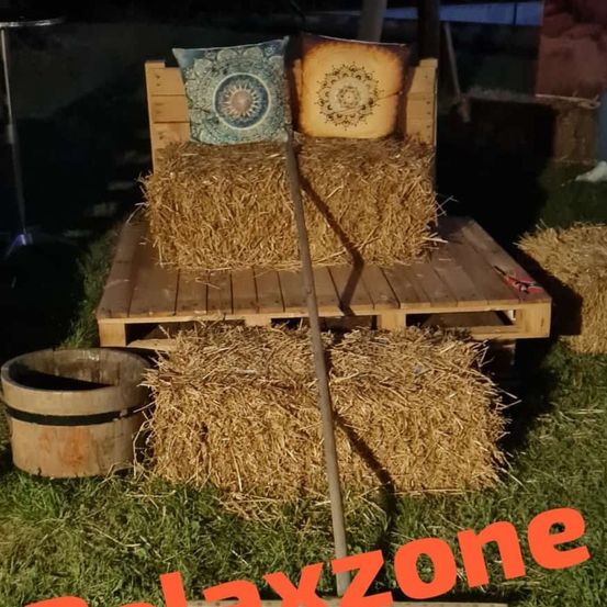 Eine rustikale Couch aus Heuballen und Paletten, mit dekorativen Kissen, auf einem Rasen bei Nacht.