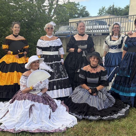 Eine Gruppe von Frauen in Vintage-Kleidern posiert an einem sonnigen Tag für ein Foto. Sie tragen alle Hüte und Handschuhe.