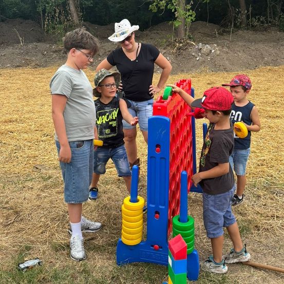 Eine Gruppe von Kindern und einer erwachsenen Frau spielen auf einem riesigen Connect Four-Brett in einem Feld.