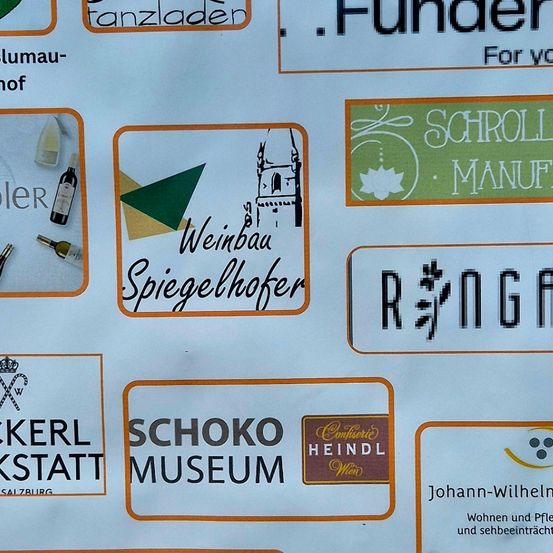 Ein Schild zeigt Unterstützer-Sponsoren wie Huber Baugmbh, Fundermax, Dopler, Weinbau Spiegelhofer, Zuckerl Werkstatt, Schoko Museum und Fashion by Katharina.