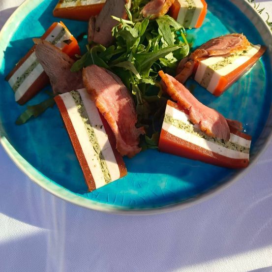 Ein blauer Teller mit verschiedenen Scheiben von Fleisch, Käse und Gemüse, garniert mit grünen Blättern auf einem weißen Tuch.