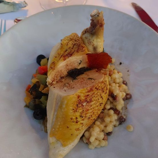 Ein Gericht aus gegrilltem Hähnchen, serviert mit Gemüse und Getreide auf einem weißen Teller.