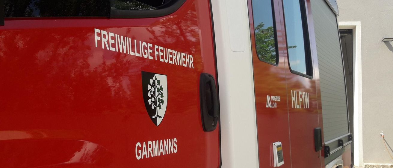 Ein rotes Fahrzeug mit weißem Rand, beschriftet mit 'Freiwillige Feuerwehr' und 'Garmanns', steht vor einem Gebäude.
