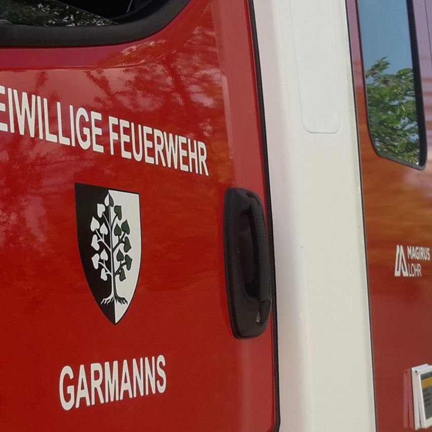 Ein rotes Fahrzeug mit weißem Rand, beschriftet mit 'Freiwillige Feuerwehr' und 'Garmanns', steht vor einem Gebäude.