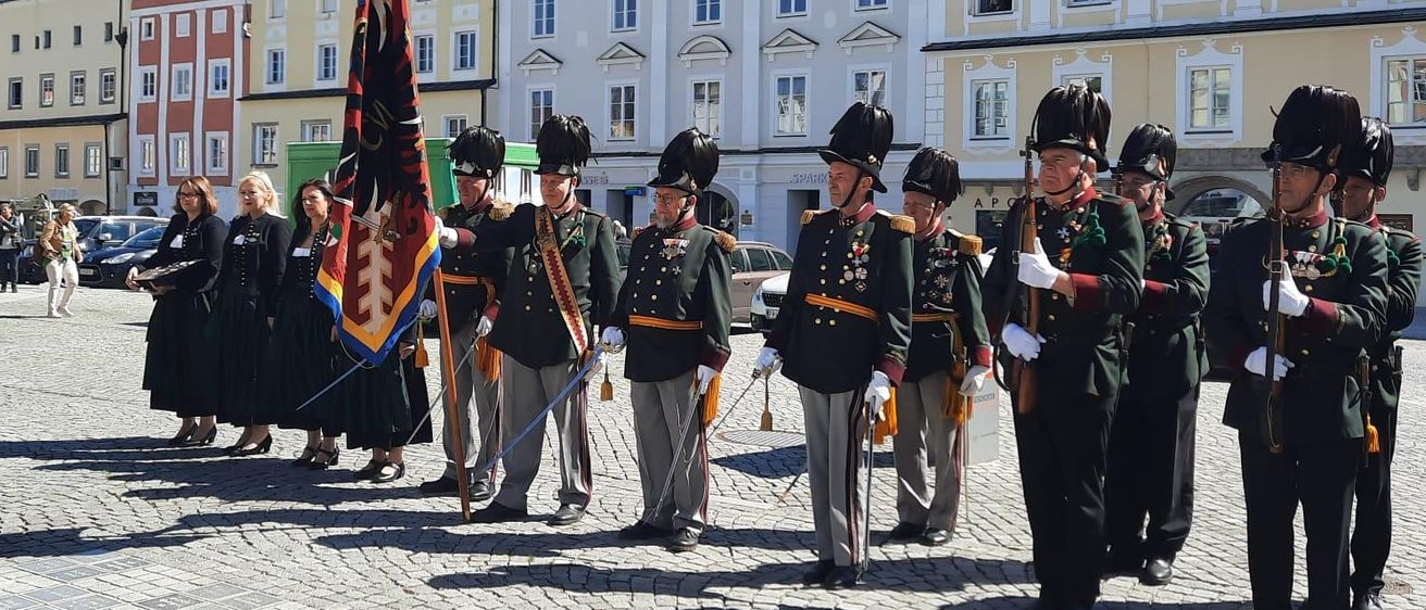 Eine Militäreinheit steht mit Schwertern und Flaggen in einer Reihe vor einem historischen Gebäude an einem sonnigen Tag.