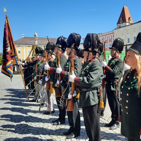 Eine Gruppe uniformierter Personen mit Gewehren steht in Formation vor einem historischen Gebäude.
