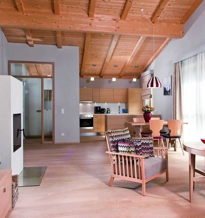 Ein offenes Wohnzimmer mit Holzböden, Decke und Möbeln. Links steht ein Kamin, rechts ein Esstisch.