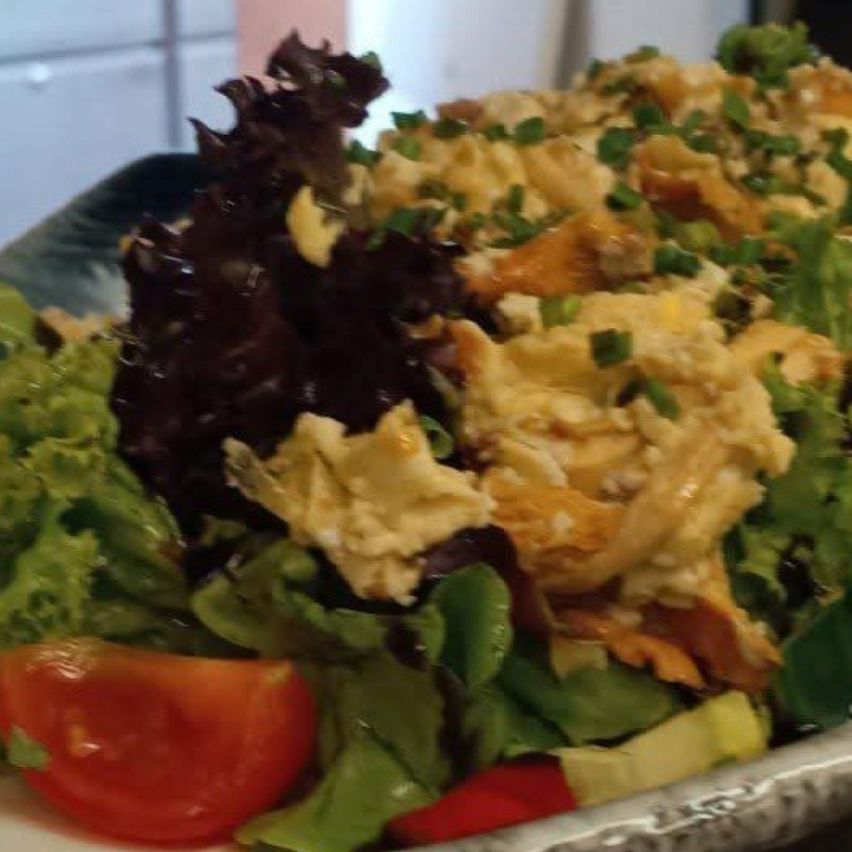 A close-up of a salad with mixed greens, a slice of tomato, and a creamy dressing.