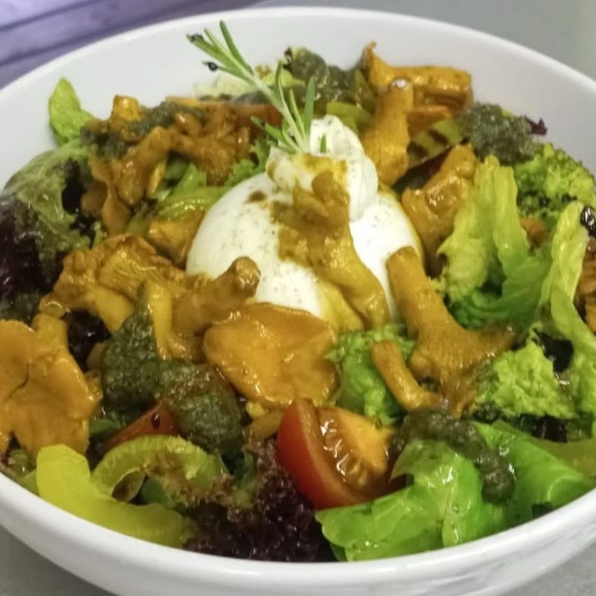 A white bowl filled with a vibrant salad featuring mixed greens, roasted mushrooms, and a poached egg topped with a creamy dressing.