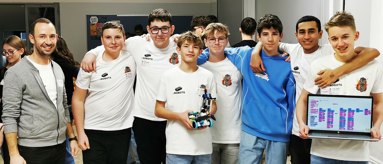 Eine Gruppe junger Menschen in weißen T-Shirts posiert für ein Foto, einer von ihnen hält einen kleinen Roboter.