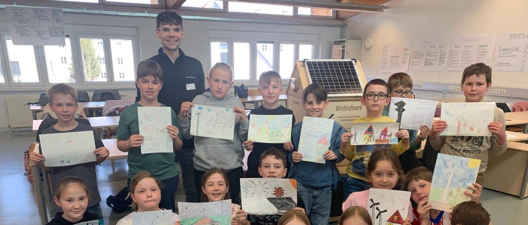 Eine Gruppe von Kindern und einem erwachsenen Mann sind in einem Klassenzimmer und halten Zeichnungen in den Händen, wahrscheinlich nehmen sie an einer Kunstaktivität oder einem Unterricht teil.