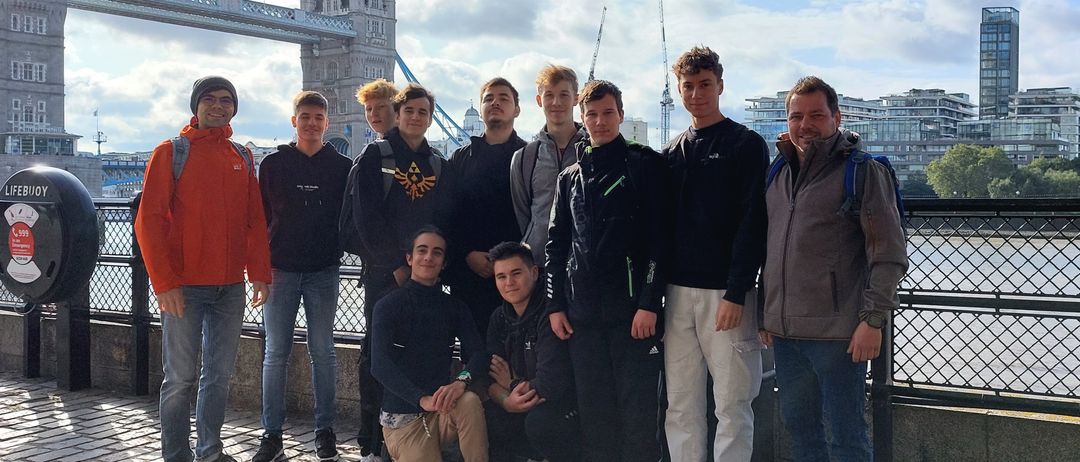 Eine Gruppe junger Männer und zwei Erwachsene posiert für ein Foto vor der Tower Bridge in London. Sie alle lächeln.