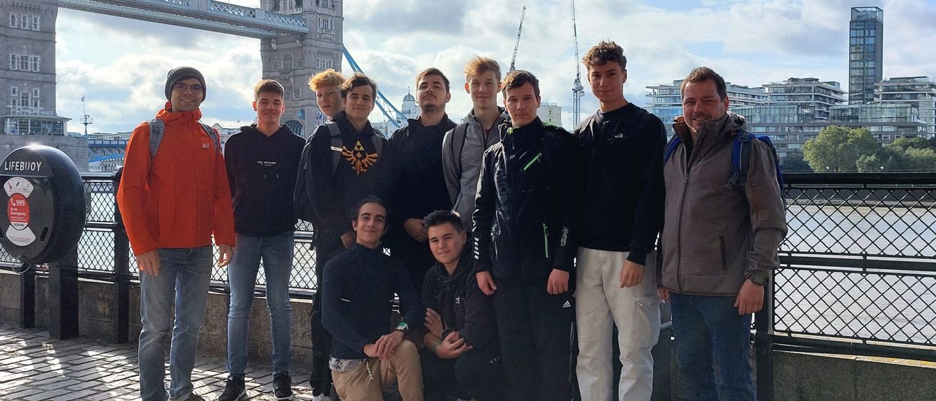 Eine Gruppe junger Männer und zwei Erwachsene posiert für ein Foto vor der Tower Bridge in London. Sie alle lächeln.