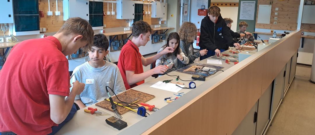 Eine Gruppe von Schülern arbeitet in einem Labor an einem Projekt. Sie verwenden Werkzeuge und Geräte auf einer Theke.