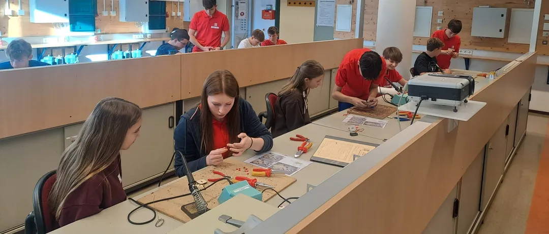Eine Gruppe von Schülern arbeitet in einer Werkstatt an einem Projekt. Sie sitzen um einen Tisch herum mit Werkzeugen und Materialien.