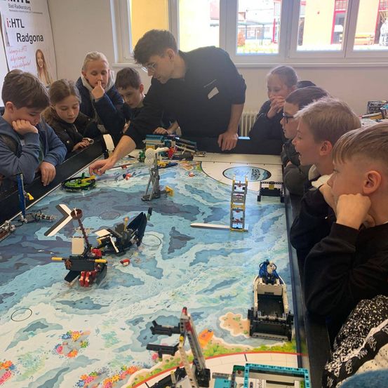 Eine Gruppe von Kindern und einem Erwachsenen betrachtet einen Tisch mit einer großen Lego-Karte und verschiedenen Lego-Schiffen.