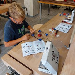 Ein junger Junge mit Brille arbeitet an einer blau-weißen Struktur auf einem Holztisch.