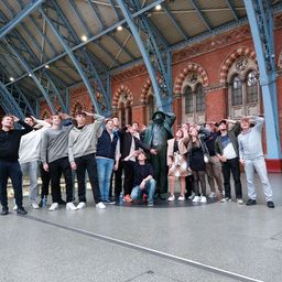 Eine Gruppe von Menschen posiert für ein Foto in einer Halle mit einer Statue in der Mitte. Sie alle lächeln und scheinen sich zu amüsieren.
