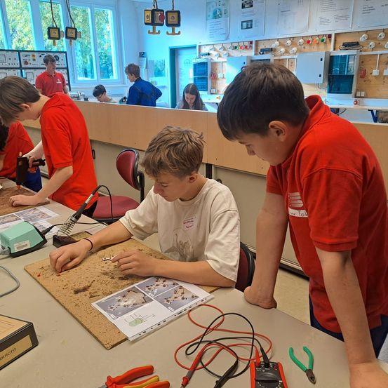 Eine Gruppe von Schülern arbeitet in einem Klassenzimmer an einem Projekt. Ein Schüler lötet, während andere beobachten.