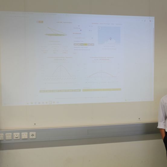 Eine weiße Leinwand zeigt eine Simulation mit Grafiken und Datenpunkten, die an einer Wand montiert ist, mit einer Person in der Nähe.