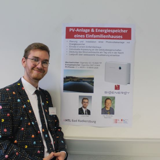 Ein Mann steht neben einem Poster mit PV-Anlage & Energiespeicher eines Einfamilienhauses. Es zeigt die Planung und Installation einer Photovoltaikanlage. Das Poster enthält Bilder eines Mannes und eines Solarstromsystems.