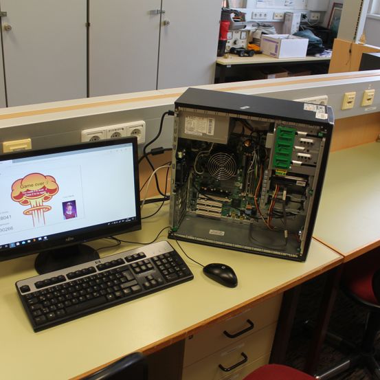 Ein Computeraufbau auf einem Schreibtisch umfasst einen Monitor, eine Tastatur und eine Maus, wobei ein geöffnetes Computergehäuse seine internen Komponenten zeigt.