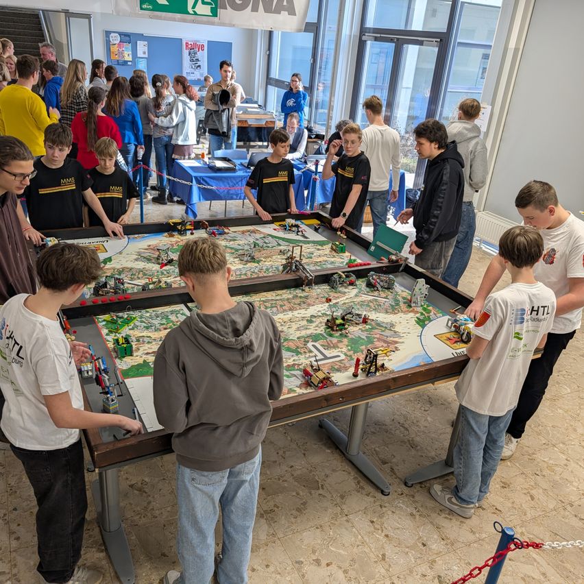 In einem Raum spielen mehrere Jungen mit Lego-Steinen auf einem großen Tisch, während andere dahinter zuschauen.