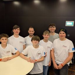 Eine Gruppe junger Männer in weißen T-Shirts mit iRobots-Logo, die in einem Raum stehen und sitzen und für ein Foto posieren.