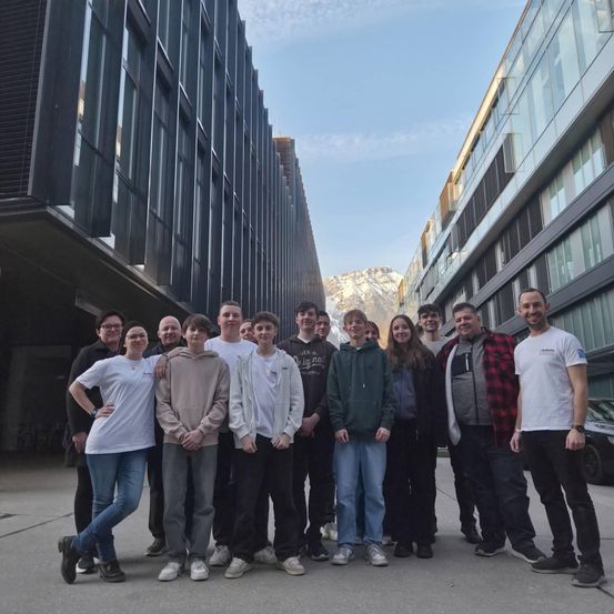 Eine Gruppe von Menschen posiert vor modernen Gebäuden, mit Bergen im Hintergrund.