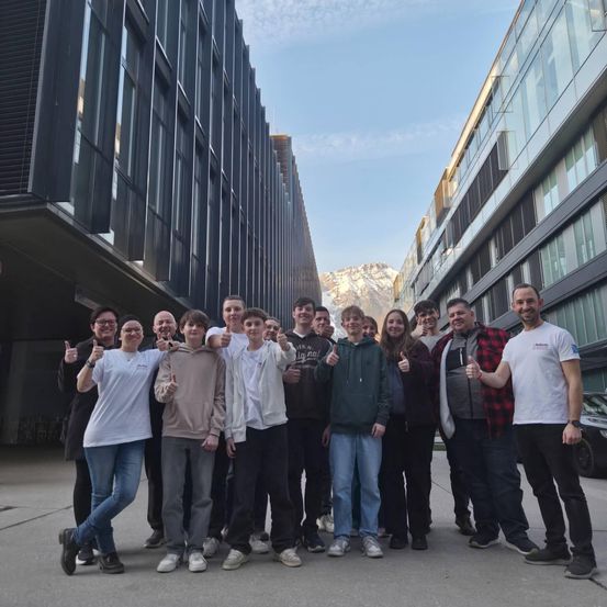 Eine Gruppe von Menschen posiert für ein Foto vor einem modernen Gebäude mit Glasfenstern, unter einem klaren blauen Himmel.